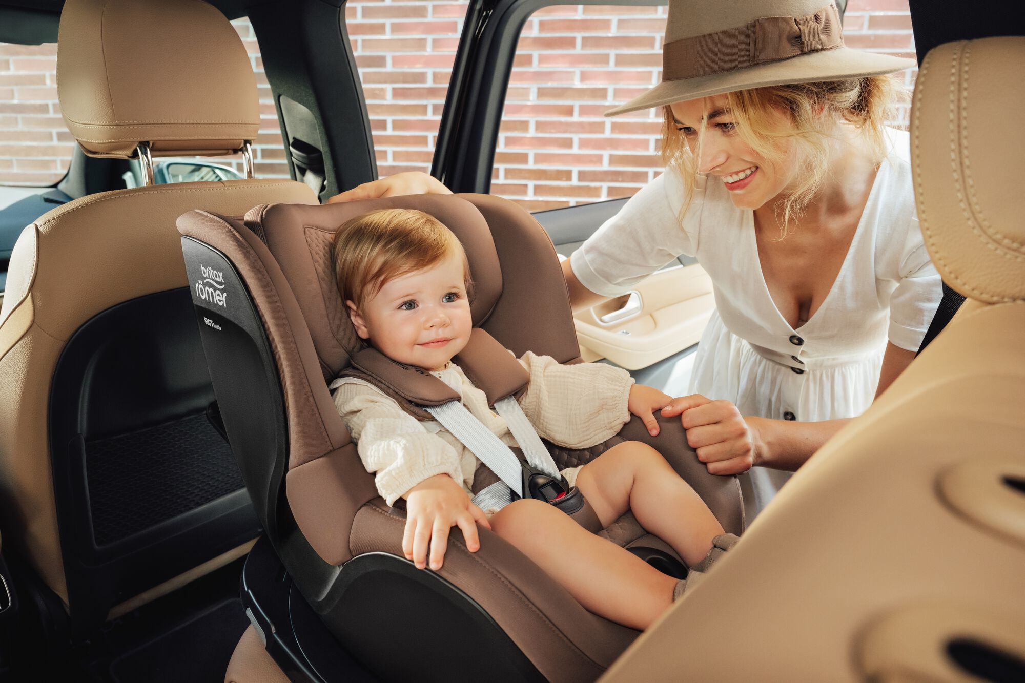 Småbarn sikret i en DUALFIX 5Z toddler car seat, med moren stående ved siden av.